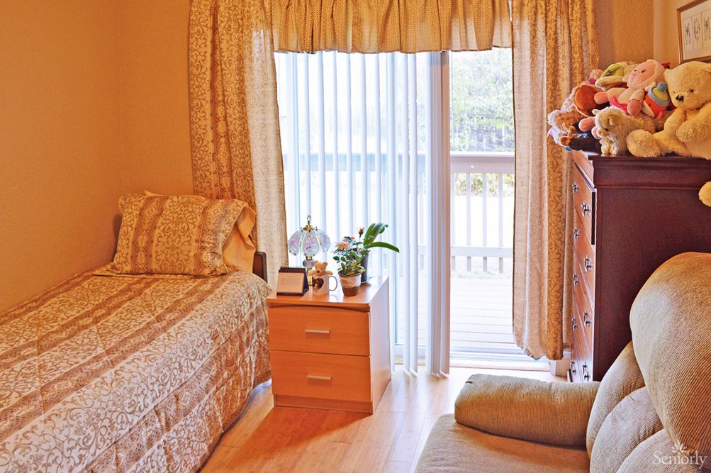A cozy bedroom with a bed, nightstand, and large window draped with curtains.