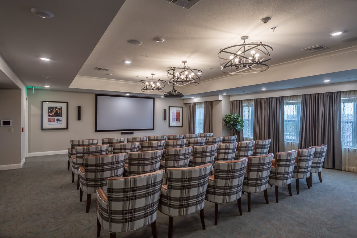 A well-appointed conference room with plaid upholstered chairs arranged in rows facing a large projection screen.