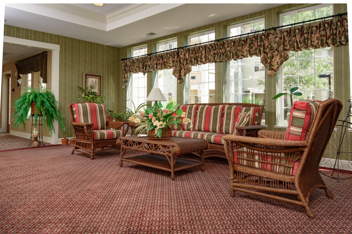A cozy living room featuring a rattan sofa set with colorful cushions, a wooden coffee table, and large windows adorned with patterned curtains.