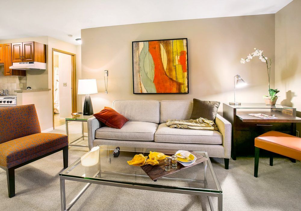 A cozy living room featuring a modern sofa, colorful abstract artwork, and a glass coffee table with decorative items.
