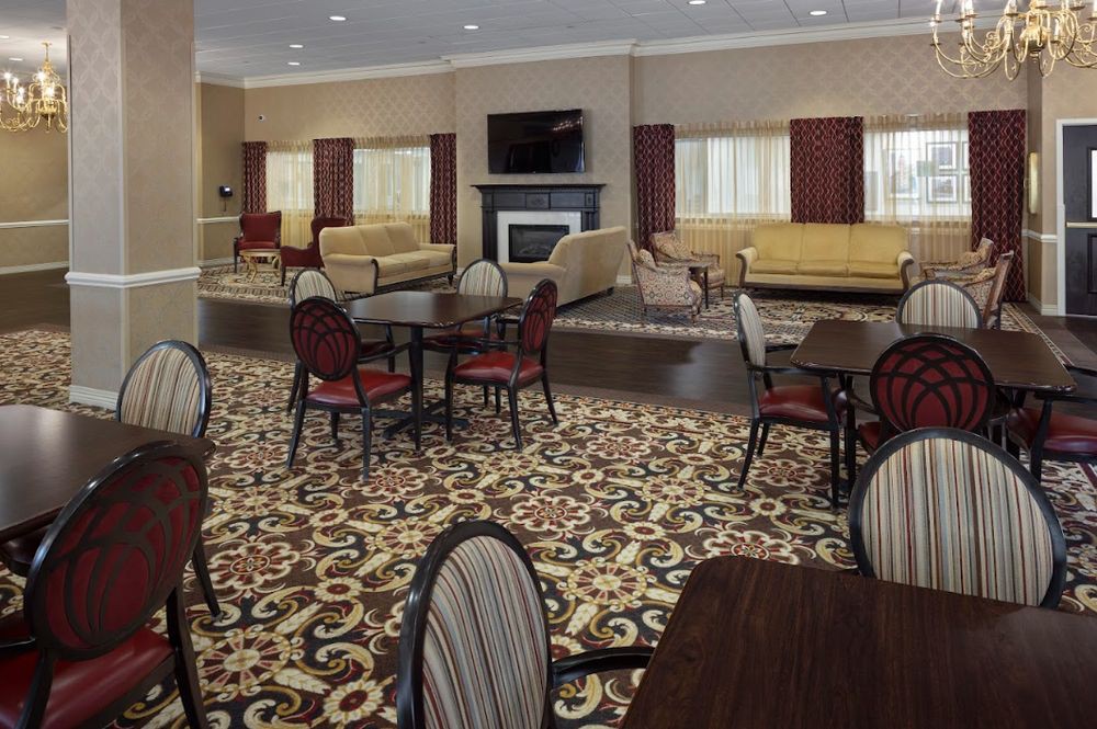 A hotel lobby with patterned carpet, multiple seating areas featuring sofas and tables, a fireplace, and a television.