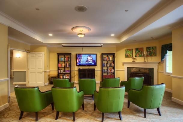 Cozy living room with green chairs, a television, bookshelves, and a fireplace.