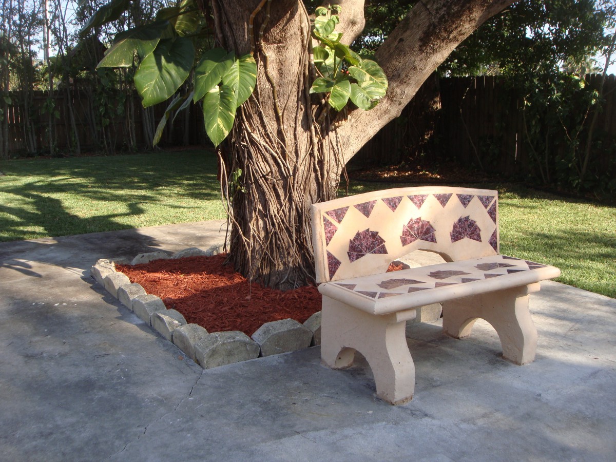 A decorative bench under the shade of a large tree in a well-maintained garden.