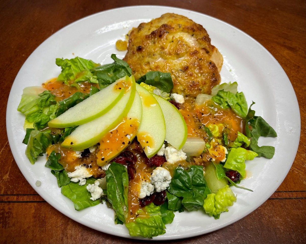 A fresh salad with apple slices, cheese, and a crab cake on a plate.