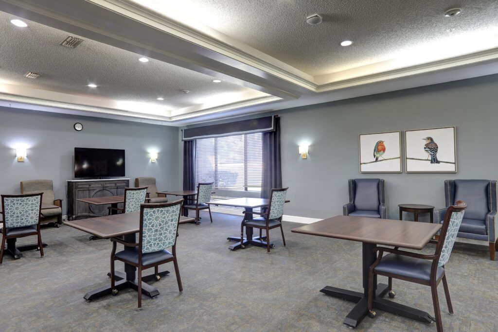 A modern dining room with tables and chairs arranged neatly, featuring ambient lighting and wall artwork.