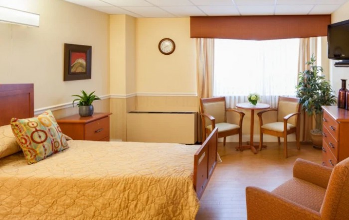 A cozy bedroom with a neatly made bed, a small table with two chairs by the window, and tasteful decor.