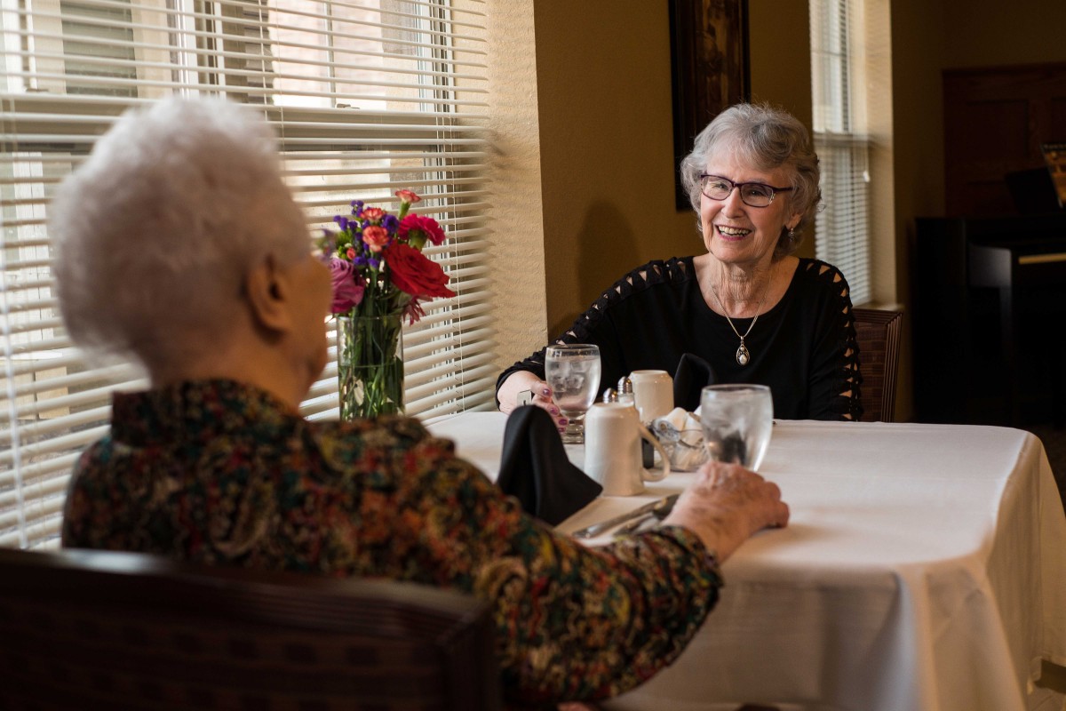 Two elderly individuals enjoying a conversation over a meal at a dining table.