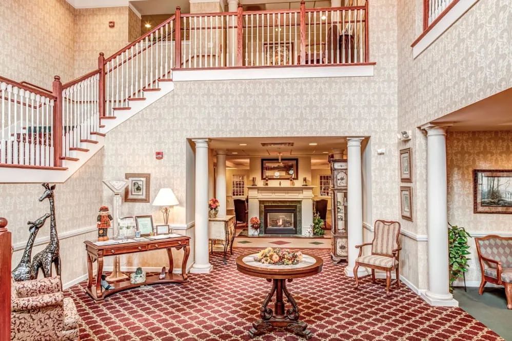 A warmly decorated lobby area featuring a fireplace, elegant furniture, and a staircase with red railings.