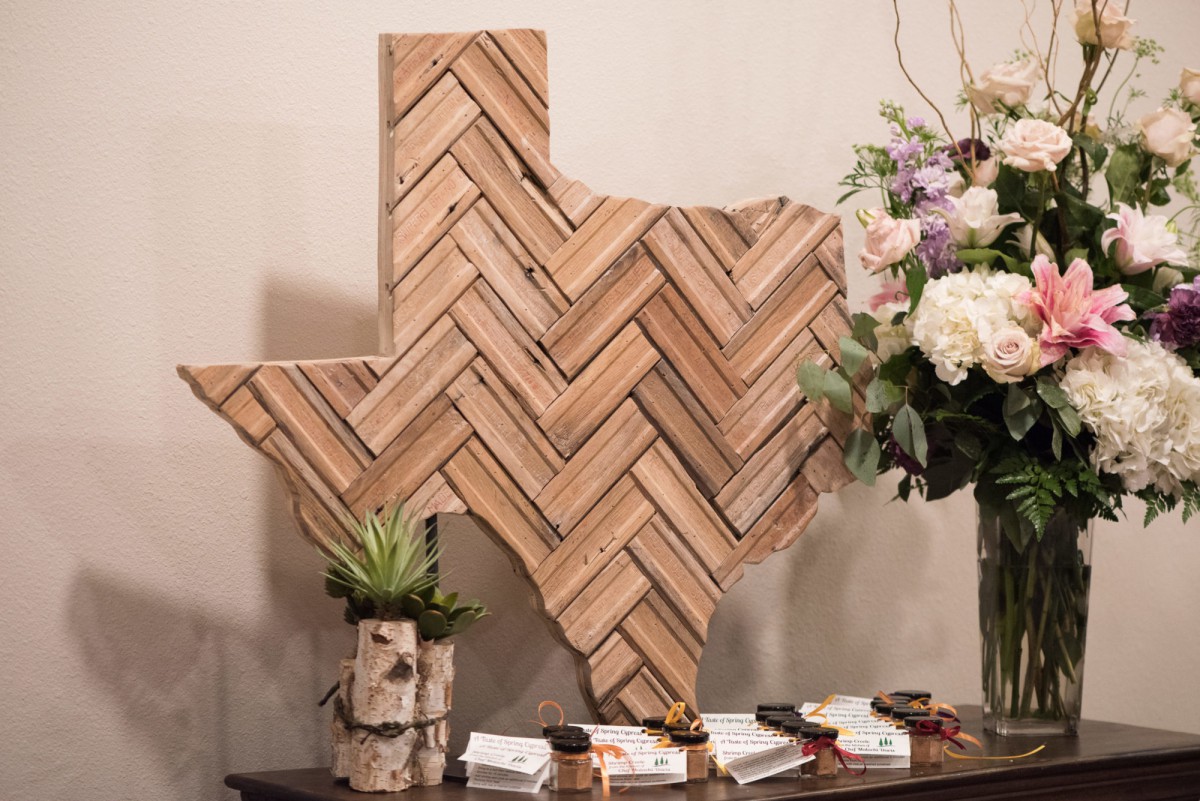Wooden herringbone pattern artwork in the shape of Texas, displayed on a table with flowers and decor items.