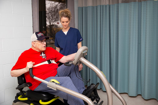 A healthcare professional assists an elderly patient with exercise equipment during a physical therapy session.