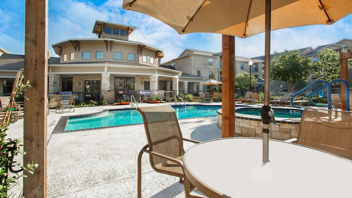 A sunny outdoor swimming pool area with patio furniture and umbrellas in a residential setting.
