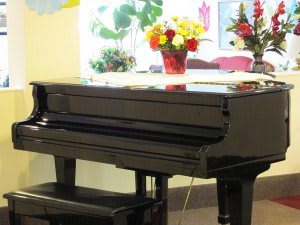 A grand piano with a vase of colorful flowers on top in a cozy room.