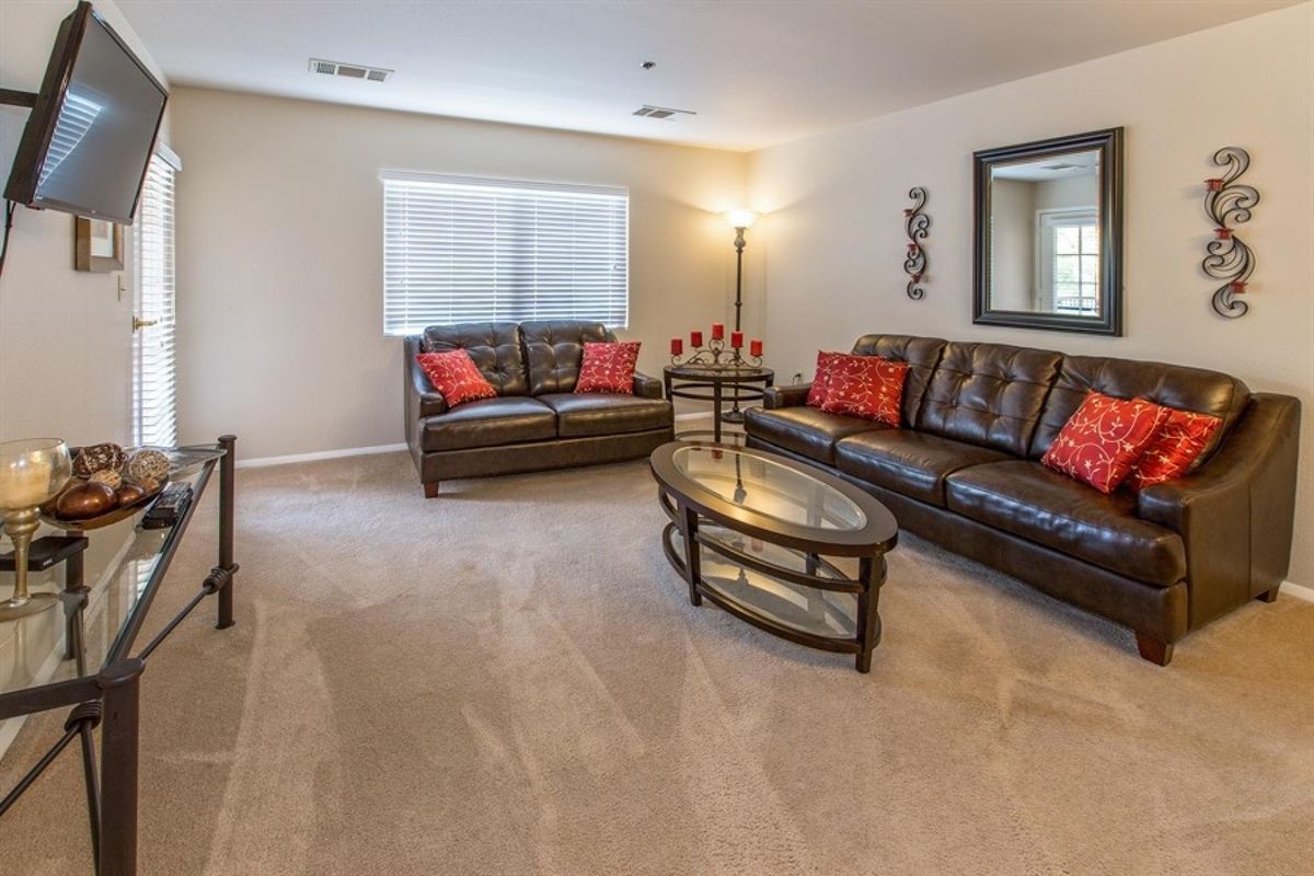 A cozy living room with leather sofas, red throw pillows, a glass coffee table, and a standing lamp.