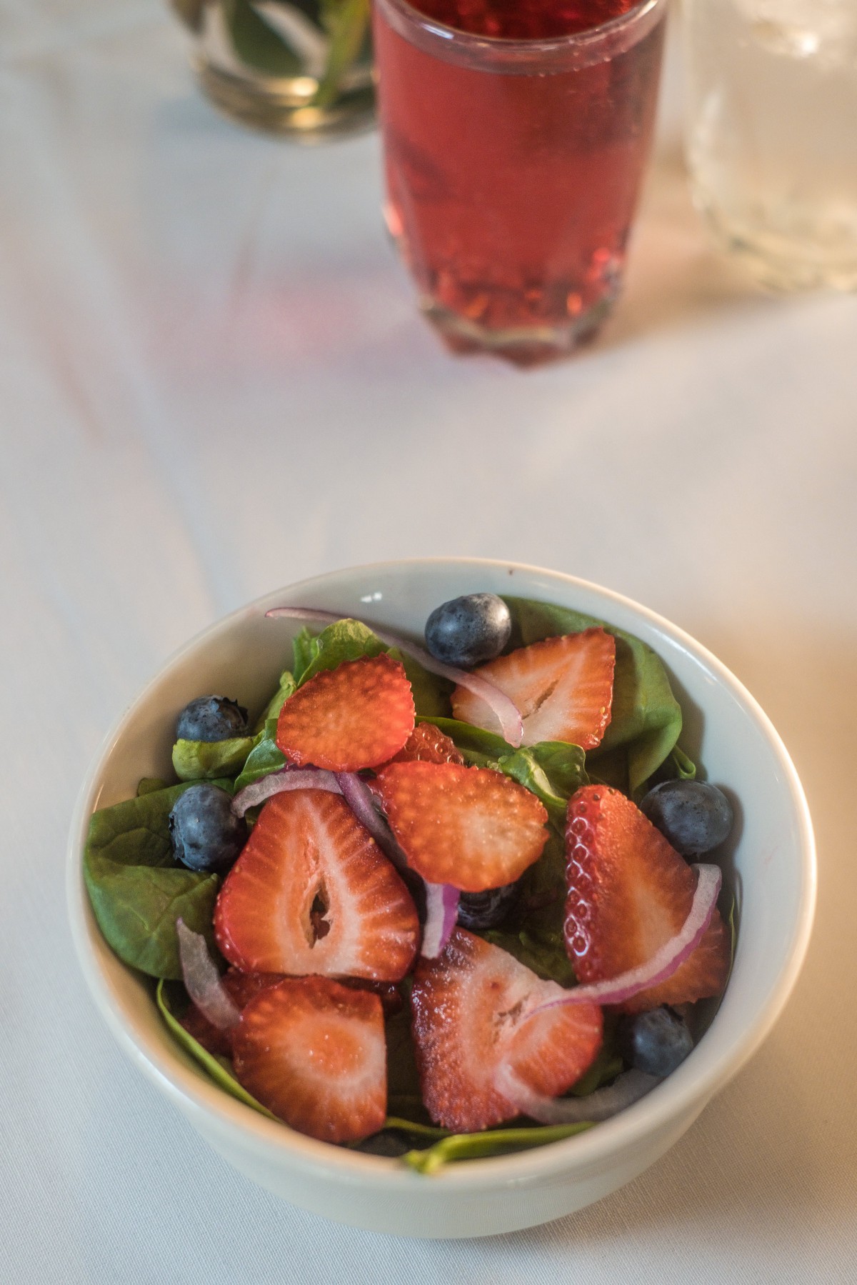 A fresh fruit salad with strawberries, blueberries, and spinach leaves.