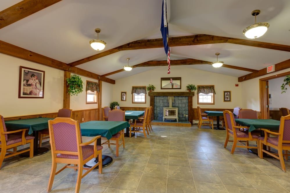 A spacious community room with tables and chairs, featuring a fireplace and a flag hanging from the ceiling.