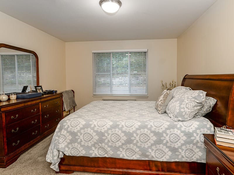 A well-decorated bedroom featuring a bed with patterned bedding, a dresser with a mirror, and a window with curtains.