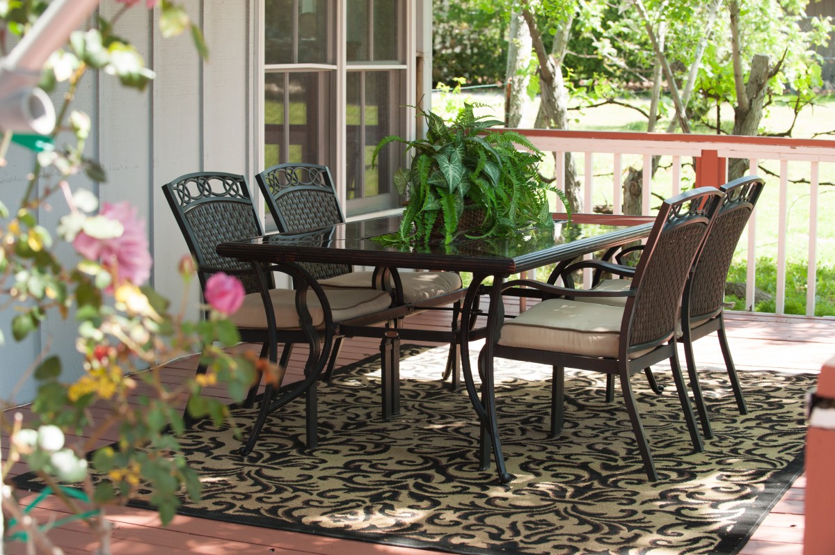 An inviting outdoor patio area with a table and chairs, decorated with plants and a rug.
