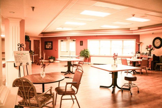 An empty dining area with tables and chairs, featuring a wooden floor and warm lighting.