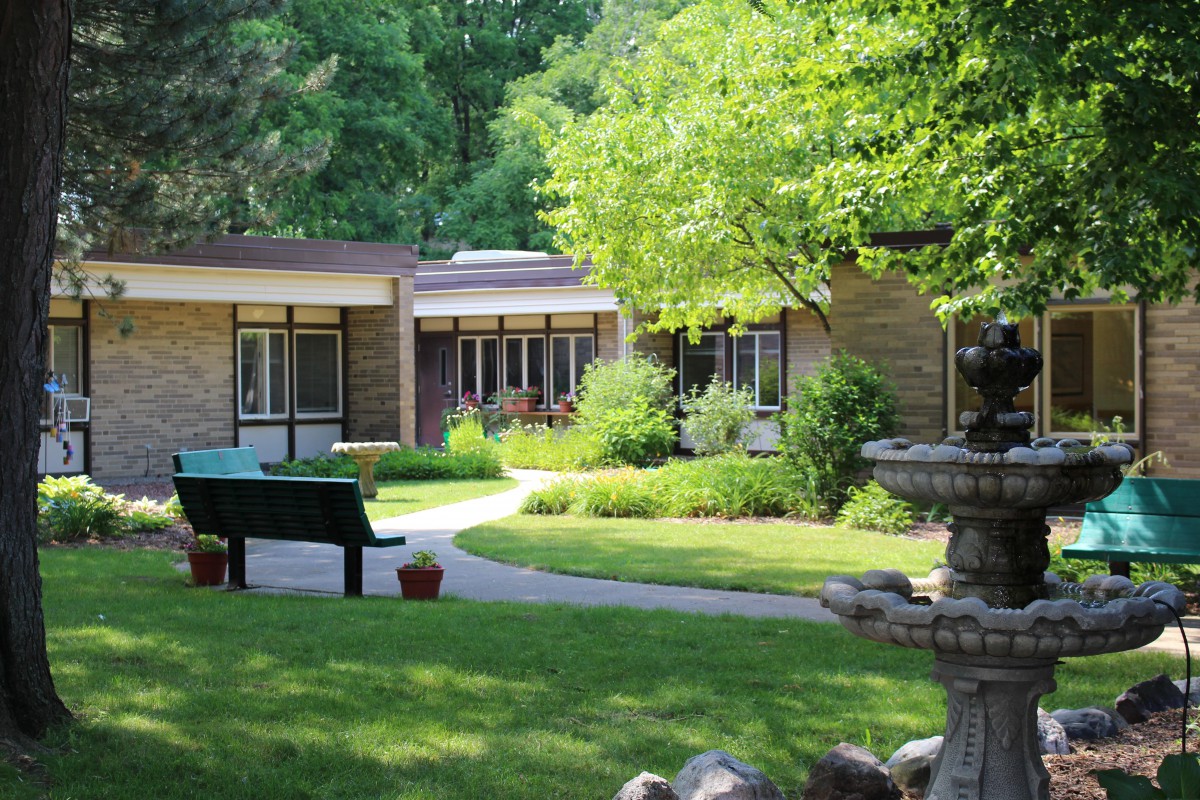 A tranquil garden setting with a fountain, surrounded by lush greenery and a modern building in the background.