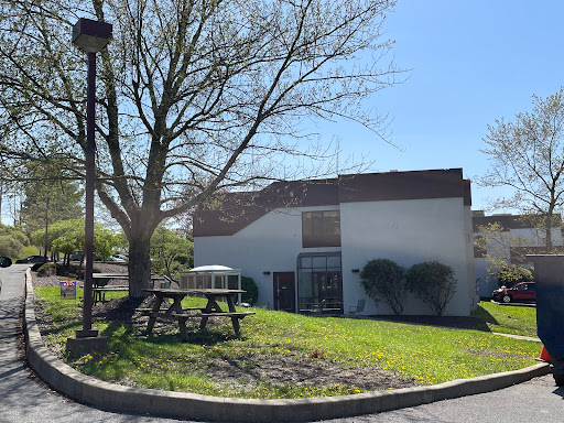 A serene outdoor view featuring a modest building surrounded by greenery and a picnic area.