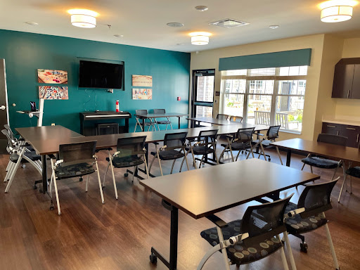 A well-lit meeting room equipped with tables, chairs, and a television for presentations.
