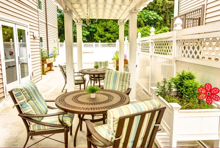 A cozy patio area with wooden tables and chairs beneath a pergola, surrounded by greenery.