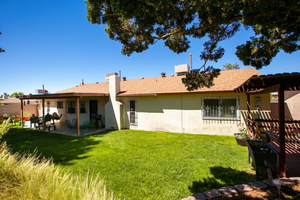 A sunny backyard of a residential house with a well-maintained lawn and surrounding trees.