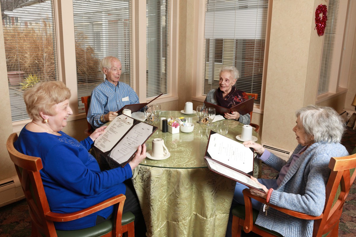 A group of seniors enjoying a meal together at a restaurant, looking at menus.