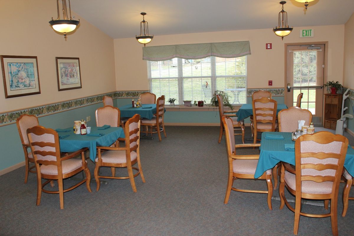 A cozy dining area with multiple tables and chairs, featuring teal tablecloths and natural light coming through the windows.