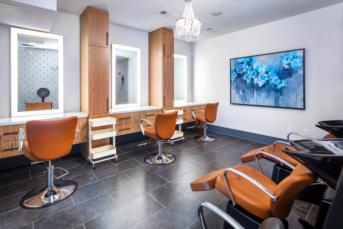 A modern salon interior with stylish hairdressing chairs, mirrors, and a decorative chandelier.