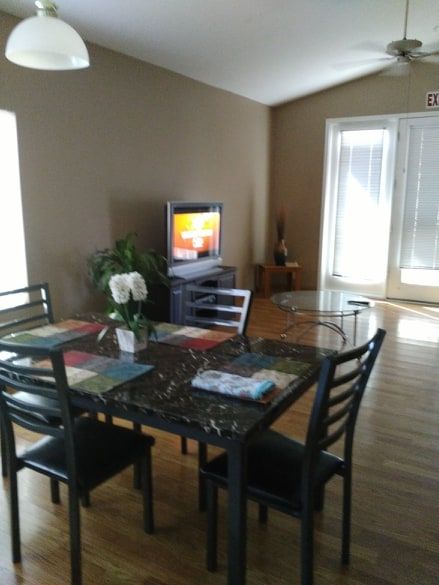 A cozy dining area with a table set, chairs, and a television in a well-lit room.