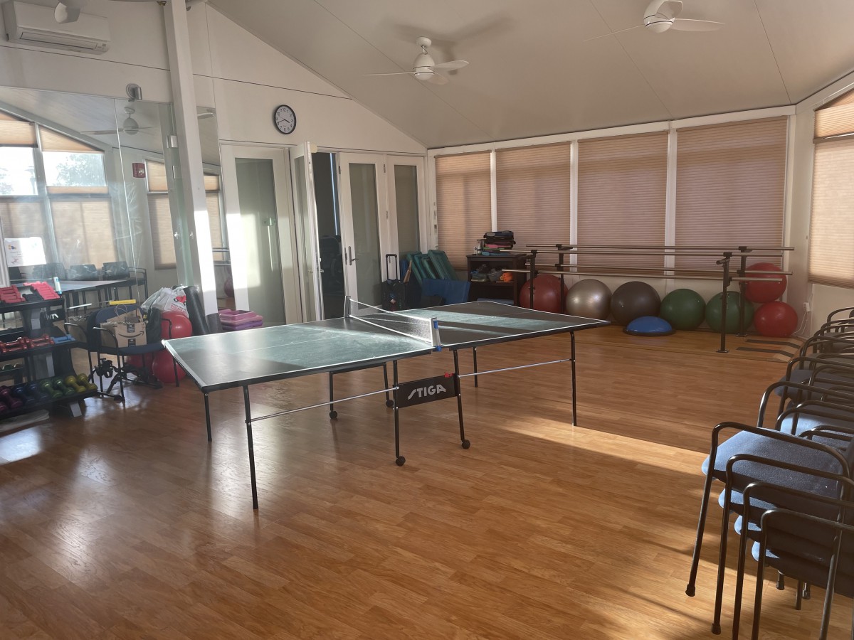 A recreation room with a table tennis setup and exercise equipment in the background.