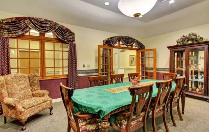 A well-furnished dining room featuring a long table with a green tablecloth, surrounded by wooden chairs, and adorned with elegant curtains and a chandelier.