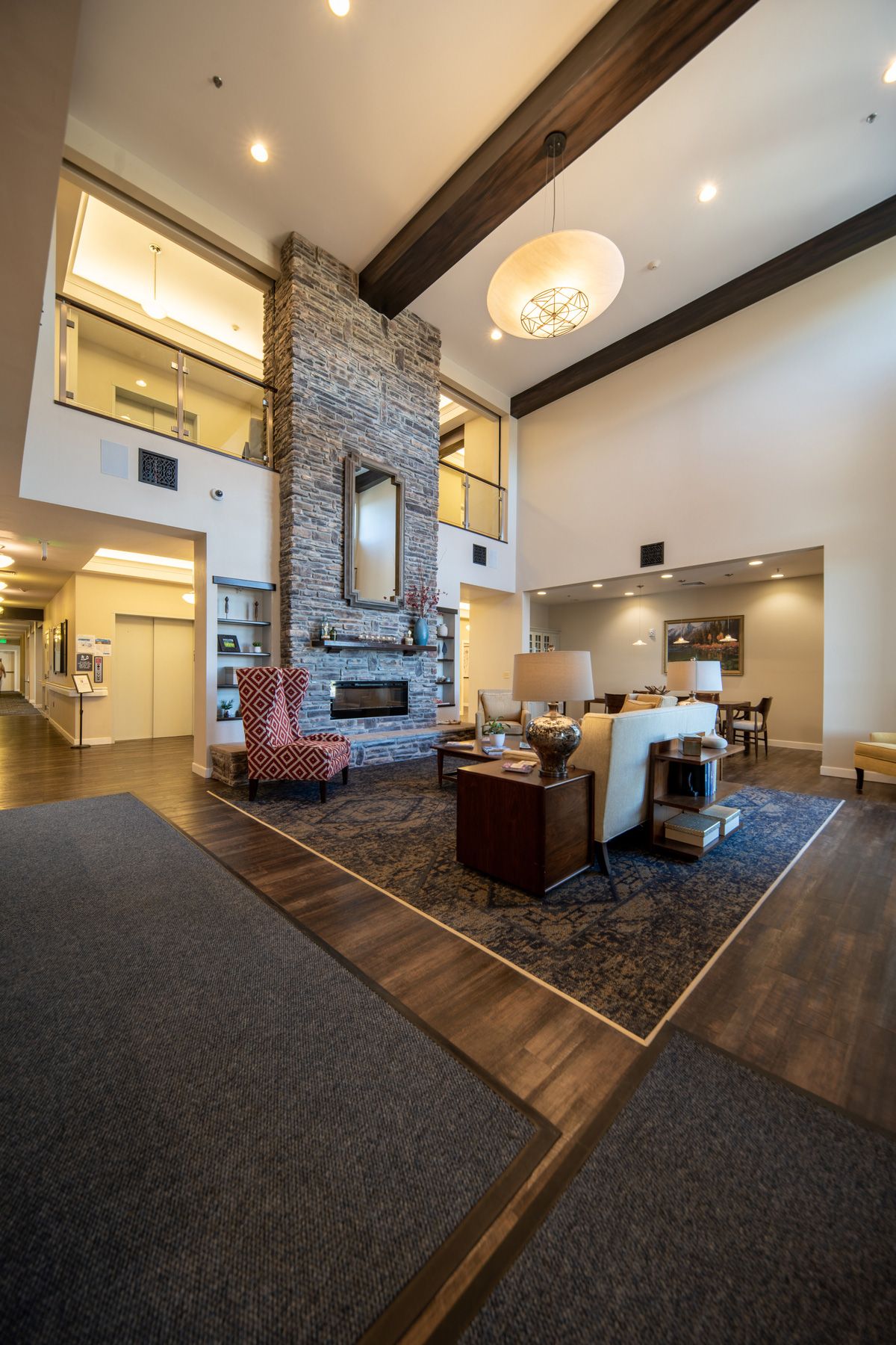 A modern lobby with a cozy seating area, featuring a stone fireplace and a high ceiling adorned with a chandelier.