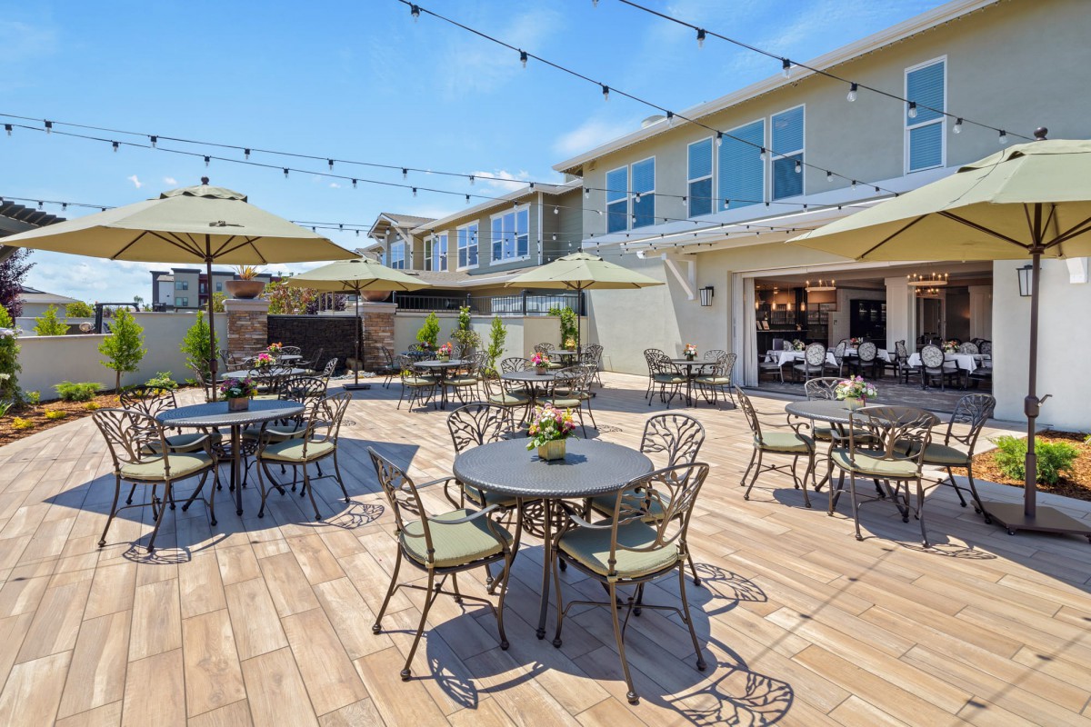 A sunny outdoor patio with tables, chairs, and umbrellas set under string lights.