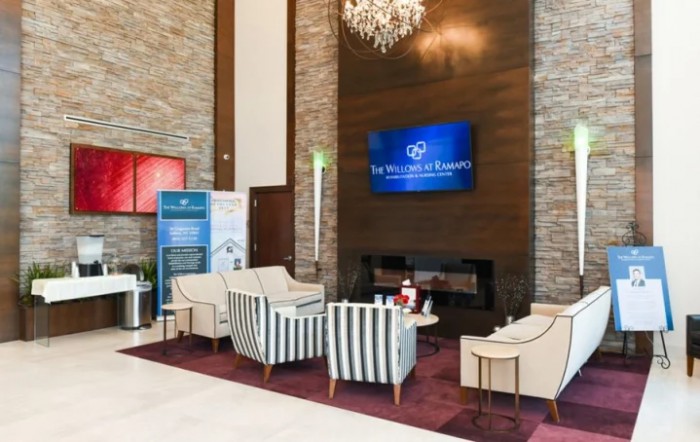 A modern hotel lobby featuring a seating area with elegant chairs, a chandelier, and a television on the wall.