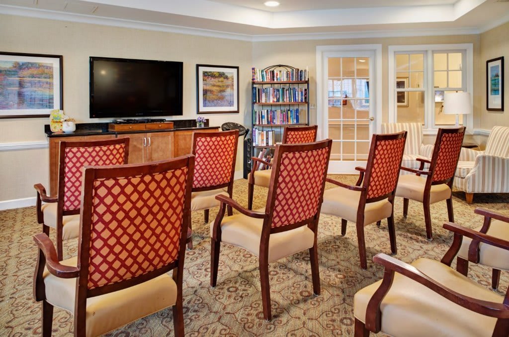 A cozy room with arranged chairs facing a television, featuring a bookshelf and carpeted flooring.