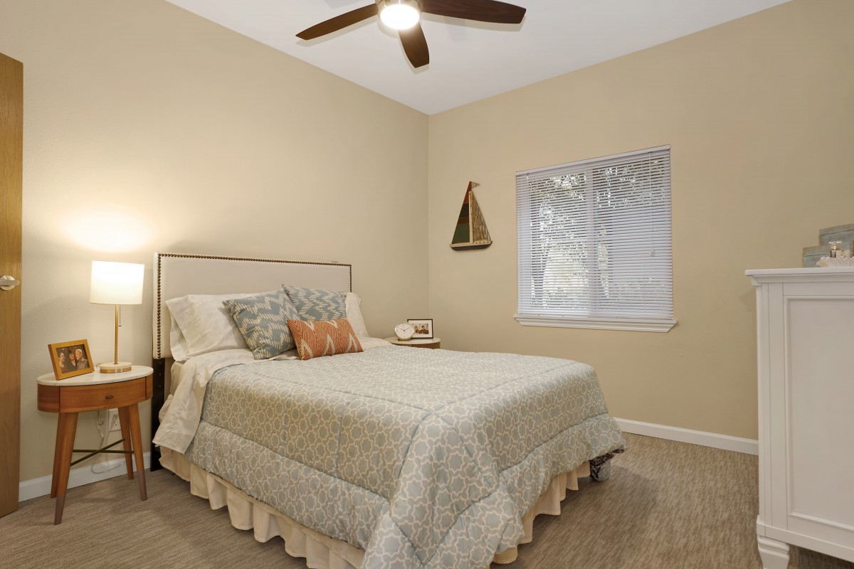 A cozy bedroom with a comfortable bed, ceiling fan, and soft lighting.