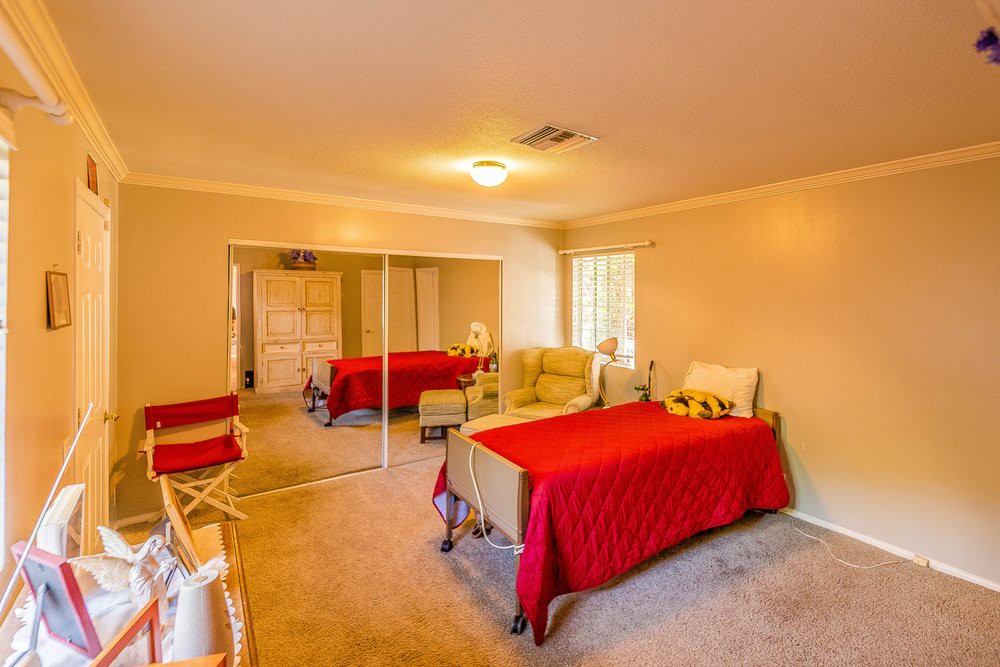 A cozy bedroom featuring a single bed with red bedding, mirrored closet doors, and warm lighting.