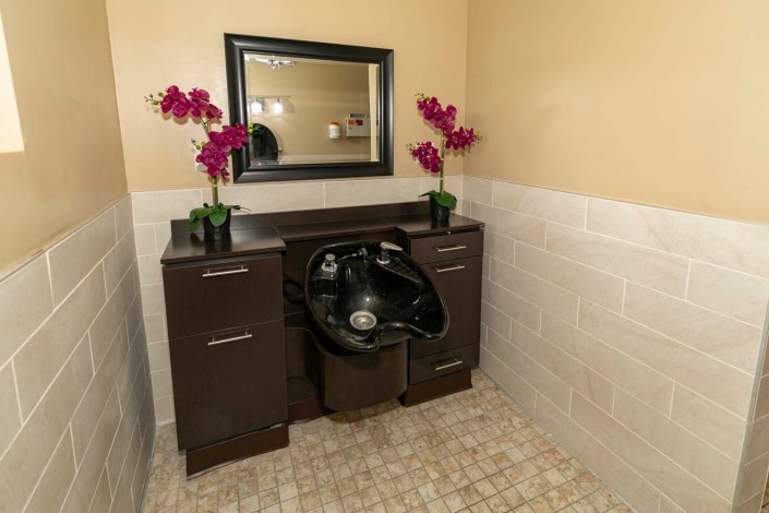 A well-equipped hair salon with a washing station featuring a sink, mirror, and decorative flowers.