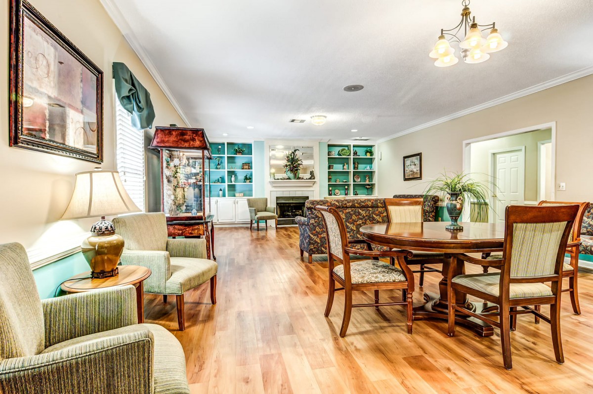 A spacious and bright living room with a dining area, featuring elegant wood flooring and classic furniture.