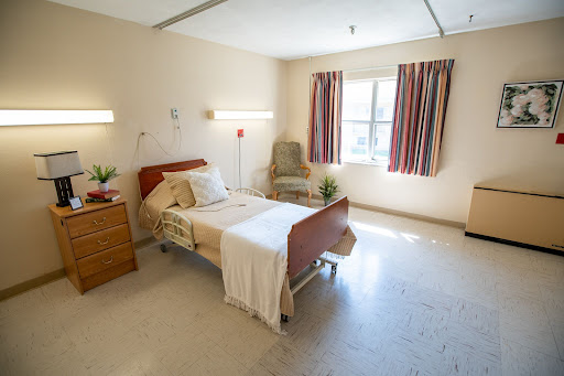 A well-lit hospital patient room featuring a bed, seating area, and window.