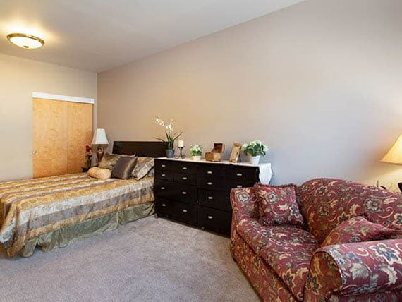 A cozy bedroom featuring a bed, dresser, and patterned sofa.