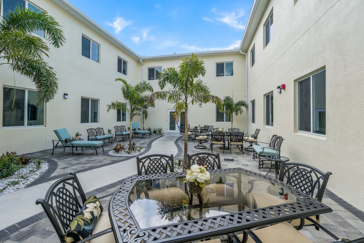 A courtyard with outdoor seating, featuring palm trees and surrounding building exterior.