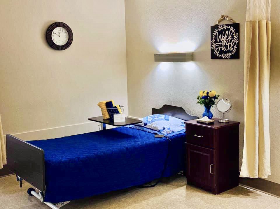 A tidy room with blue bedding and a nightstand decorated with flowers.