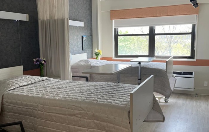 A peaceful hospital room with two beds and a window letting in natural light.