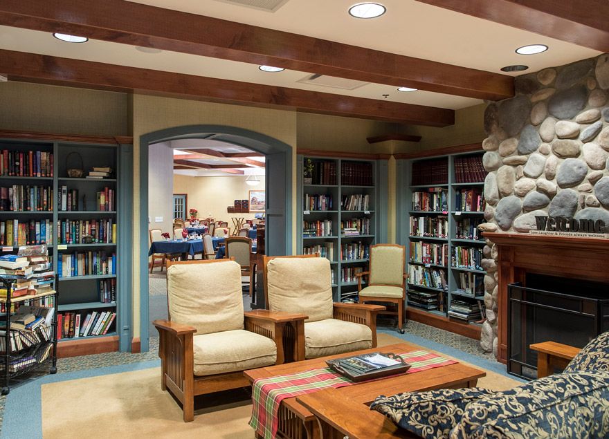 A cozy library room with bookshelves, armchairs, and a fireplace.