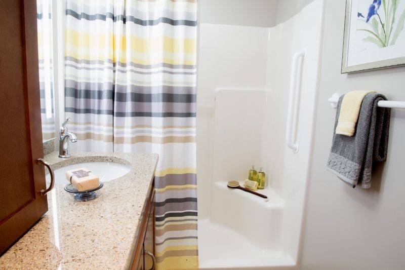 A modern bathroom with a striped shower curtain, a sink with a granite countertop, and various toiletries.