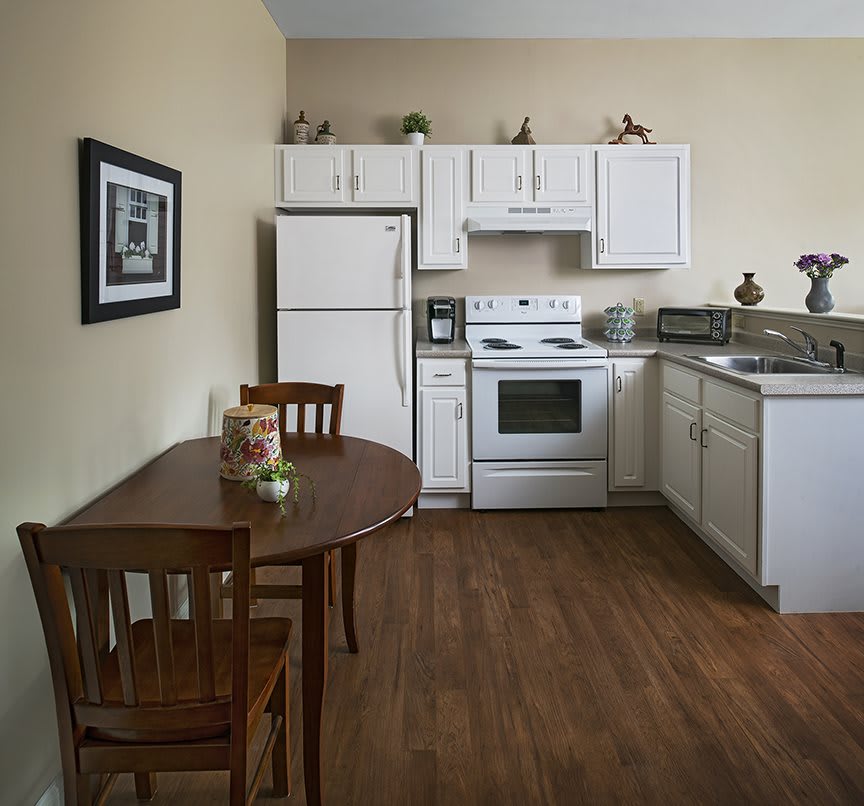 A cozy kitchen with a wooden dining table and chairs, featuring white cabinets, a refrigerator, and an electric stove.
