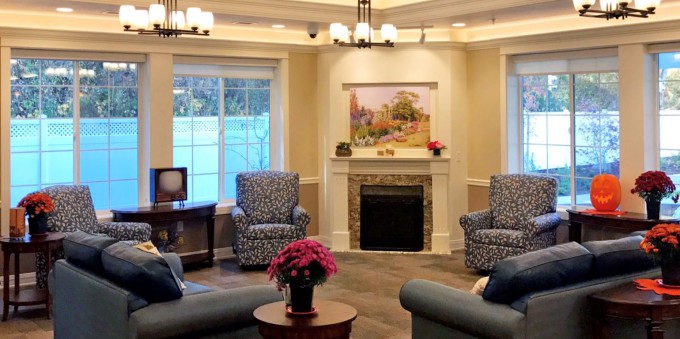A cozy living room with comfortable seating arranged around a fireplace, featuring tasteful decor and a landscape painting above the mantel.